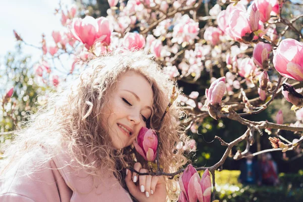 Rizado dulce chica huele la fragante magnolia rosa en el parque, un montón de sol y calor — Foto de Stock