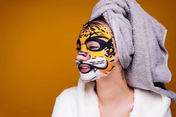 Смішна молода дівчина з рушником на голові хоче бути красивою, на її обличчі зволожуюча маска з леопардовими сварками — стокове фото