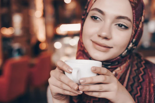 Seorang gadis Arab yang menarik dengan kerudung di kepalanya menikmati kopi harum, tersenyum dan bermimpi tentang sesuatu — Stok Foto