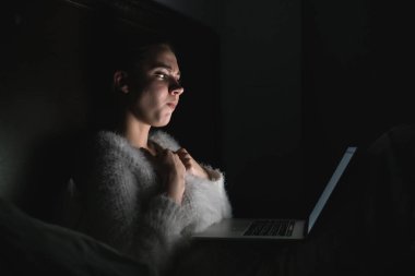 karanlıkta onun laptopunda bir korku filmi izlerken gece geç saatte yatakta oturan genç korkmuş kız