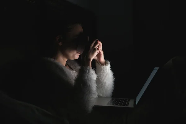 젊은 여 자가 침대에 저녁에 앉아, 그녀의 노트북에 영화를 보고 차를 마시고 — 스톡 사진