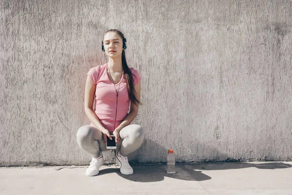 Мирна жінка в рожевій футболці, що відпочиває після бігу, слухаючи музику на навушниках — стокове фото