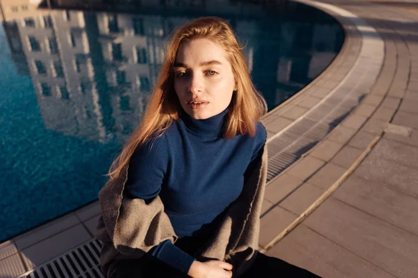 Luxurious confident girl blonde resting by the pool in the sun, posing, in a blue sweater — Stock Photo, Image