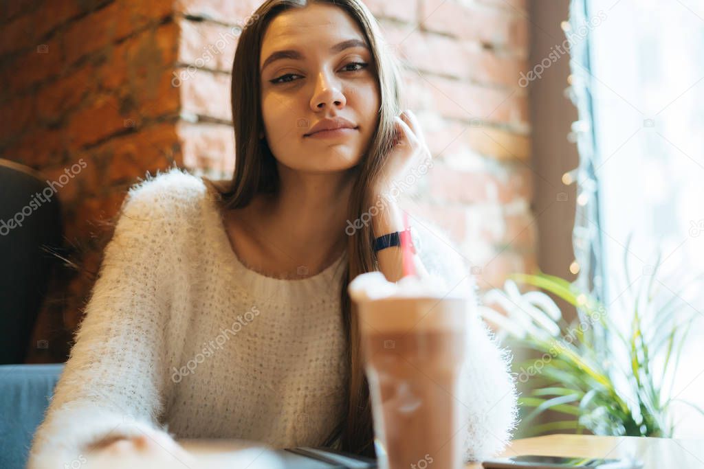 confident beautiful girl freelancer in a white sweater resting in a cafe after work