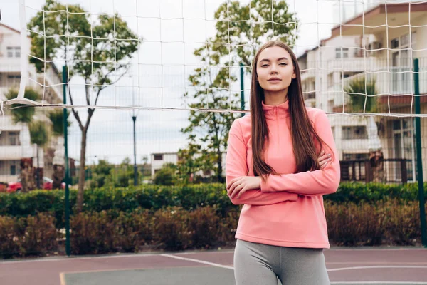 Mooi slank meisje in een roze jas rustend op een sportveld, graag spelen volleybal — Stockfoto