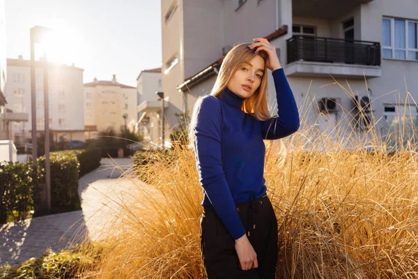 Jonge blonde model meisje in blauwe trui poseren in de zon buiten stralen — Stockfoto