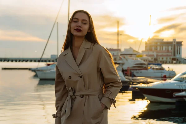 Hermosa chica atractiva con el pelo largo posando en el puerto, en abrigo beige — Foto de Stock