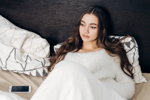 Hermosa chica con el pelo largo se encuentra en la cama bajo una manta blanca, quiere dormir — Foto de Stock