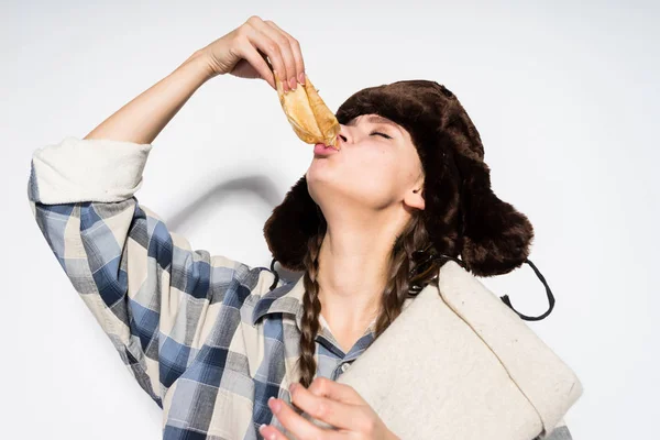 Hungrige Russin mit schwarzem Hut isst eifrig heiße Pfannkuchen, feiert Fastnacht — Stockfoto