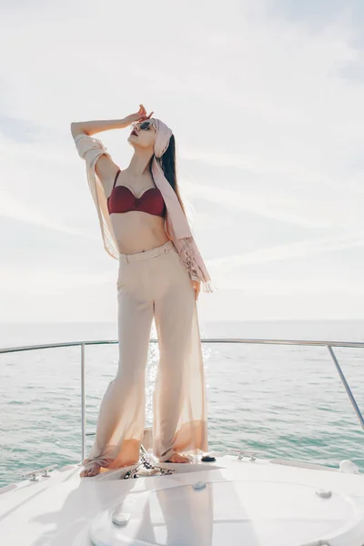 Una chica de lujo con ropa elegante y ligera posando en un yate al sol, navegando a las islas —  Fotos de Stock