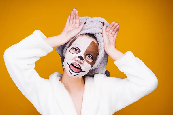 Roztomilá dívka v bílém županu pózuje na obličejovou masku s tlamy psa — Stock fotografie