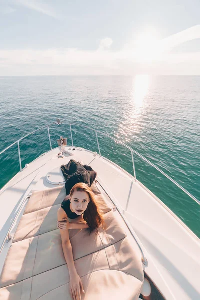 Роскошная привлекательная девушка в черной одежде лежит на яхте, позирует, наслаждается отдыхом — стоковое фото