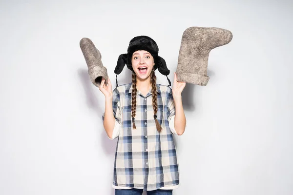 Fröhliche junge Russin mit Zöpfen freut sich im Winter, hält Filzstiefel in den Händen — Stockfoto