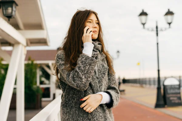 Красива брюнетка дівчина гуляє по міських вулицях в похмурий день, розмовляючи по телефону — стокове фото