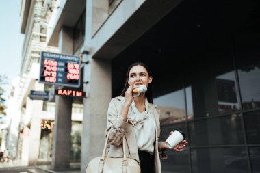 İşçi iş için acele ve üstünde belgili tanımlık gitmek yiyor, sokakta kahve içer