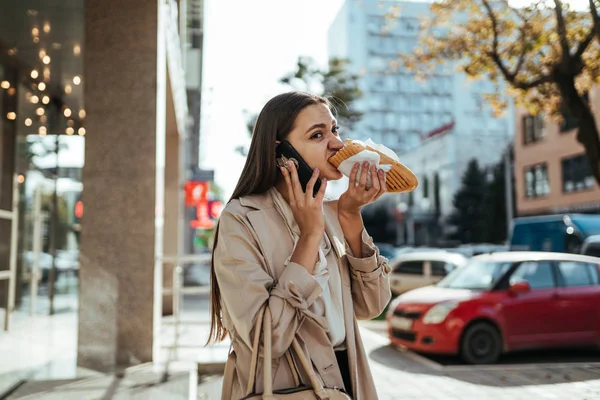 Стрессовая офисная женщина ест по дороге и разговаривает по телефону на улице — стоковое фото