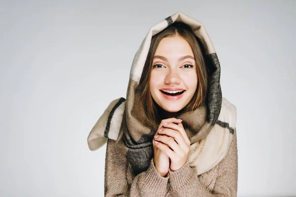 Eine schöne junge Frau, in einen Schal gehüllt, wärmt ihre Hände und lächelt, isoliert auf weiß. Winterporträt — Stockfoto