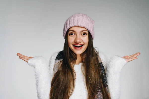 Eine junge Frau in Winterkleidung und Hut, breitet überrascht die Arme aus, kann keine Wahl treffen — Stockfoto