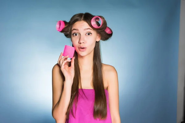 Woman on a blue background in curlers holds a pink box in hands — ストック写真