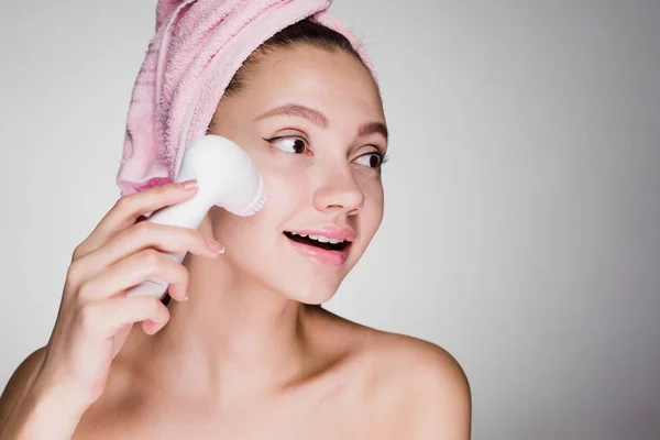 Une femme avec une serviette sur la tête effectue un nettoyage en profondeur de son visage avec une brosse électrique — Photo