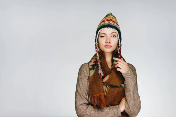 Jovem mulher alegre em um chapéu quente escandinavo e cachecol em um fundo branco levantou uma sobrancelha com surpresa e descrença — Fotografia de Stock