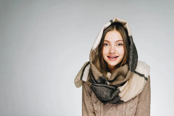 Schönes Mädchen in einen beigen Schal gehüllt lächelnd über weißem Hintergrund — Stockfoto