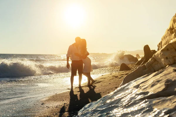Счастливая молодая пара, стоящая на песчаном пляже на закате — стоковое фото