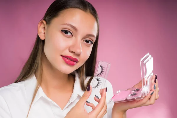 Mädchen steht auf rosa Hintergrund hält falsche Wimpern in den Händen — Stockfoto