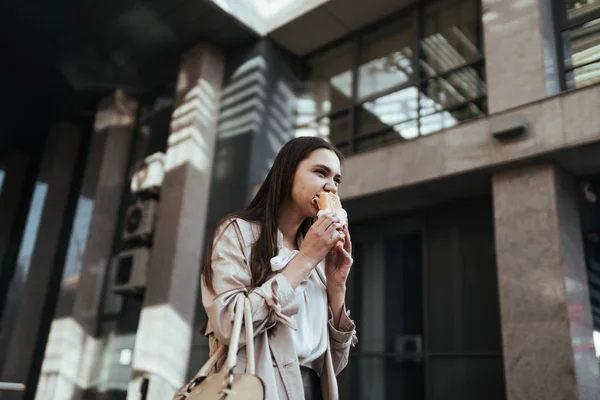 Young beautiful woman rushing and having lunch on the go outside, eating a sandwich, mouthful of food — Stock Photo, Image