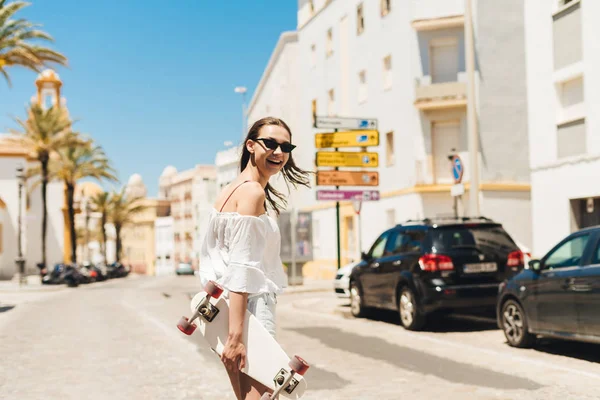 Una joven estudiante con un patín en las manos se da la vuelta y se ríe. Ciudad Vieja de Europa, vacaciones —  Fotos de Stock