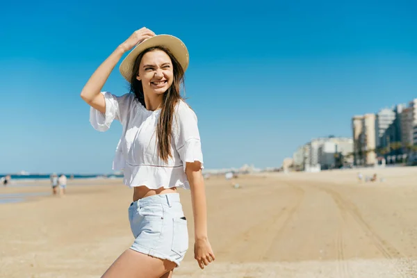 Feliz mujer joven de moda en un sombrero está descansando en la playa sobre el fondo del océano. Vacaciones en el resort — Foto de Stock