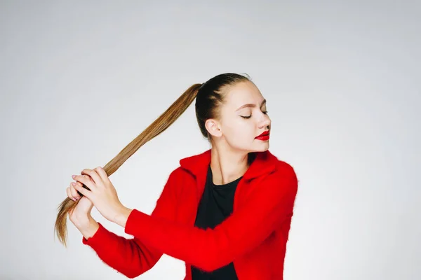 Chica de moda en una chaqueta roja se sostiene por la cola sobre un fondo blanco, estudio — Foto de Stock