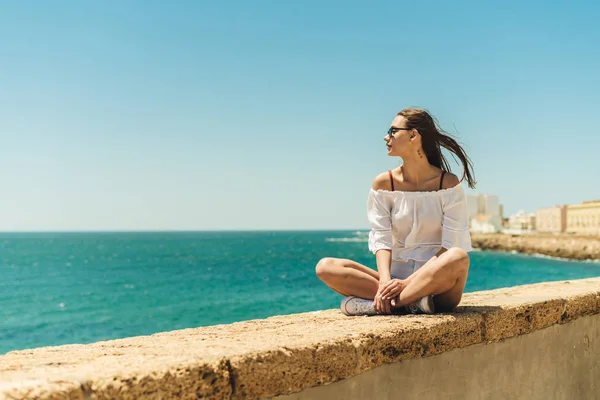 En ung flicka sitter på bakgrunden av havet, sommar, sol, semester på studenten. Enkel resa — Stockfoto