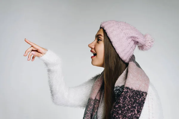 Chica sorprendida en ropa de invierno mira hacia otro lado y muestra algo con un dedo . — Foto de Stock