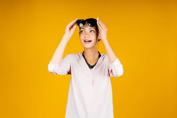 Surprised tourist girl lifts her sunglasses in surprise, on a yellow background