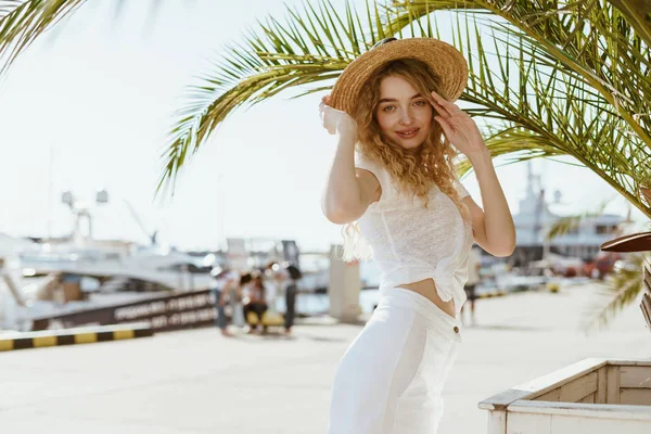 Hermosa chica sexy en un traje blanco y sombrero de paja se encuentra entre las palmeras — Foto de Stock