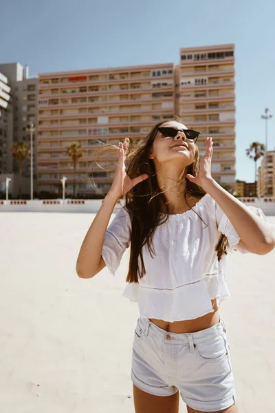 Menina em roupas brancas na praia reúne seu cabelo no vento — Fotografia de Stock