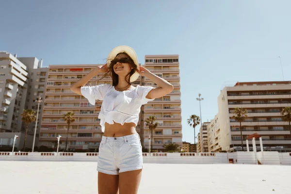 Feliz chica bronceada en vacaciones sosteniendo sombrero, viento fuerte, arena blanca, vacaciones —  Fotos de Stock
