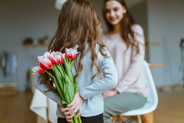 Blick von hinten, ein kleines Mädchen hält einen Strauß Tulpen hinter ihrem Rücken und schenkt ihrer Mutter. Muttertag — Stockfoto