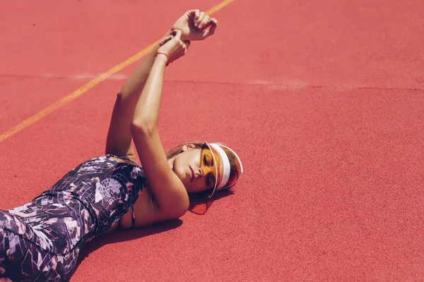 Sports fashion woman lying on a red background, on her head a yellow tennis cap from the sun