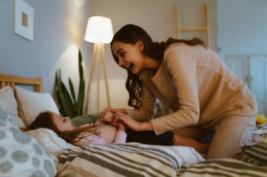 Bej süveter giyen tatlı anne gıdıklanıyor ve yatak odasına küçük bir kız koyuyor.