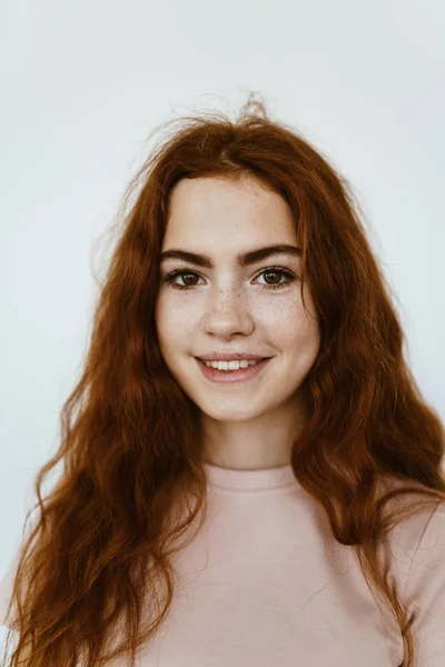 Adorable joven con el pelo rojo trenzado rizado con pecas en su cara en el fondo blanco en la camiseta de color rosa pálido sonrisas lindas — Foto de Stock