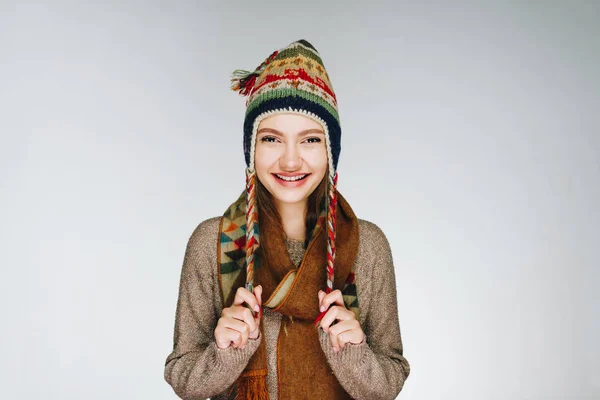 Geweldig jong meisje met de Scandinavische stijl hoed en bruine sjaal op de witte achtergrond in een bruine trui schattige glimlach — Stockfoto