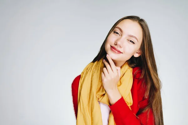 Atractiva joven con el pelo largo oscuro en un suéter rojo con una bufanda amarilla sobre un fondo blanco es hasta algo — Foto de Stock
