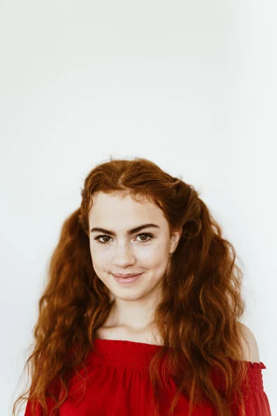 Rapariga atraente com cabelo encaracolado vermelho amarrado em rabo de cavalo, com sardas no rosto na camisola vermelha no fundo branco, sorrindo bonito — Fotografia de Stock