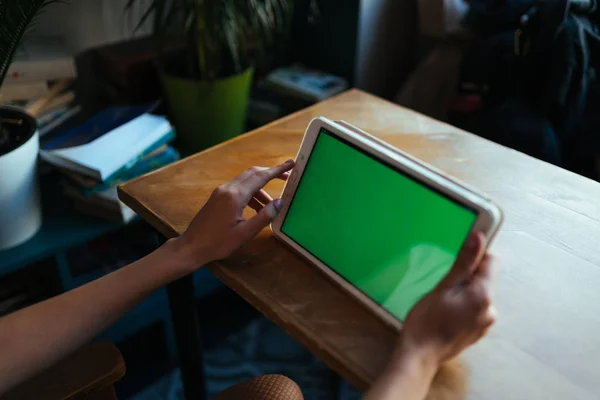 Kobiece dłonie trzymają tabletkę z zielonym ekranem na stole w kawiarni. makieta — Zdjęcie stockowe
