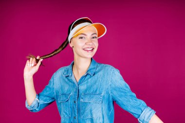 Öğrenci kafasında şapkayla sevinçle gülümsüyor, kendini at kuyruğundan tutuyor. arkaplan pembe