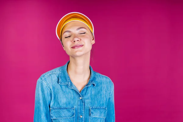 Buena chica en una visera con los ojos cerrados. emoción de placer. sobre un fondo rosa — Foto de Stock