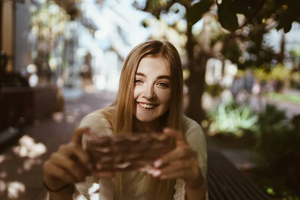 Flicka i solen med ett leende tar bilder på telefonen — Stockfoto
