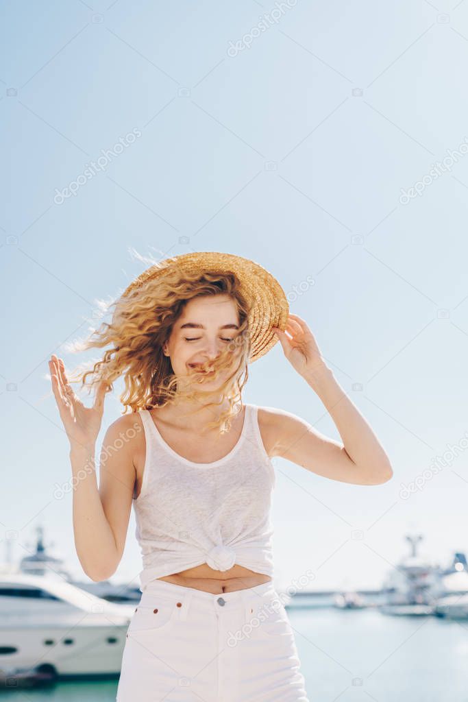 girl in a hat stands in the wind against the background of ships